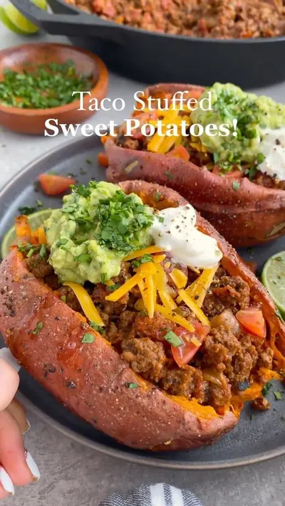 Twee met taco-gehakt gevulde zoete aardappelen op een bord, gegarneerd met guacamole, zure room en verse koriander.