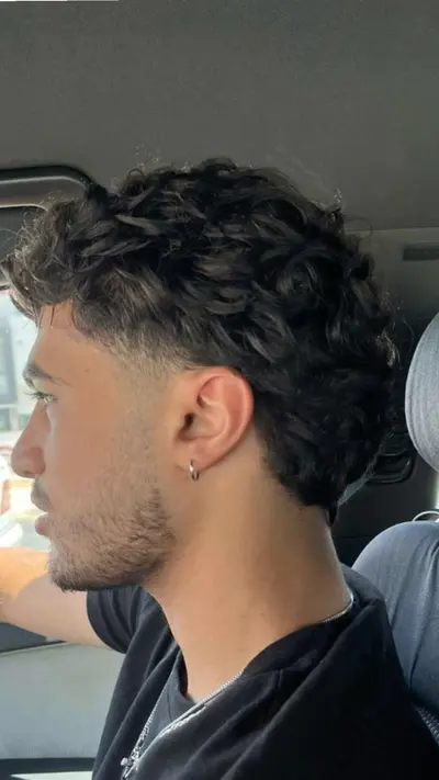 Seitenprofil eines jungen Mannes im Auto mit dunklem, lockigem Deckhaar und einem sauber rasierten Fade an den Seiten.
