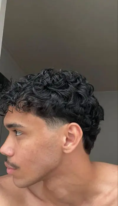 Profilansicht eines jungen Mannes mit voluminösen dunklen Locken und einem präzisen Fade-Schnitt.