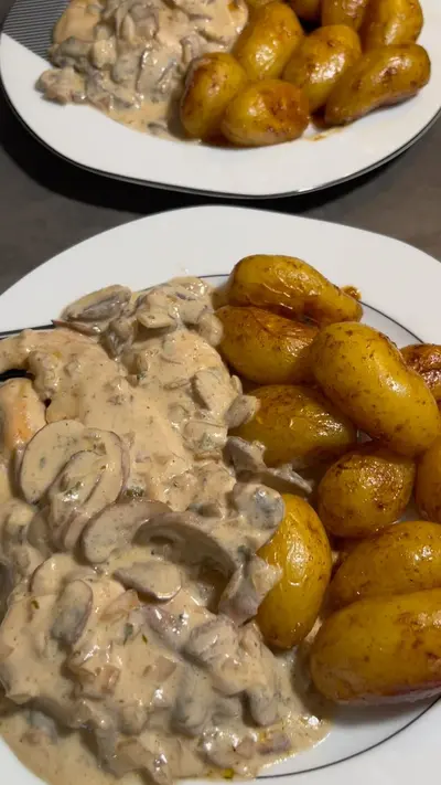 Deux assiettes de poulet aux champignons nappé de sauce crème avec des pommes de terre grenailles dorées.