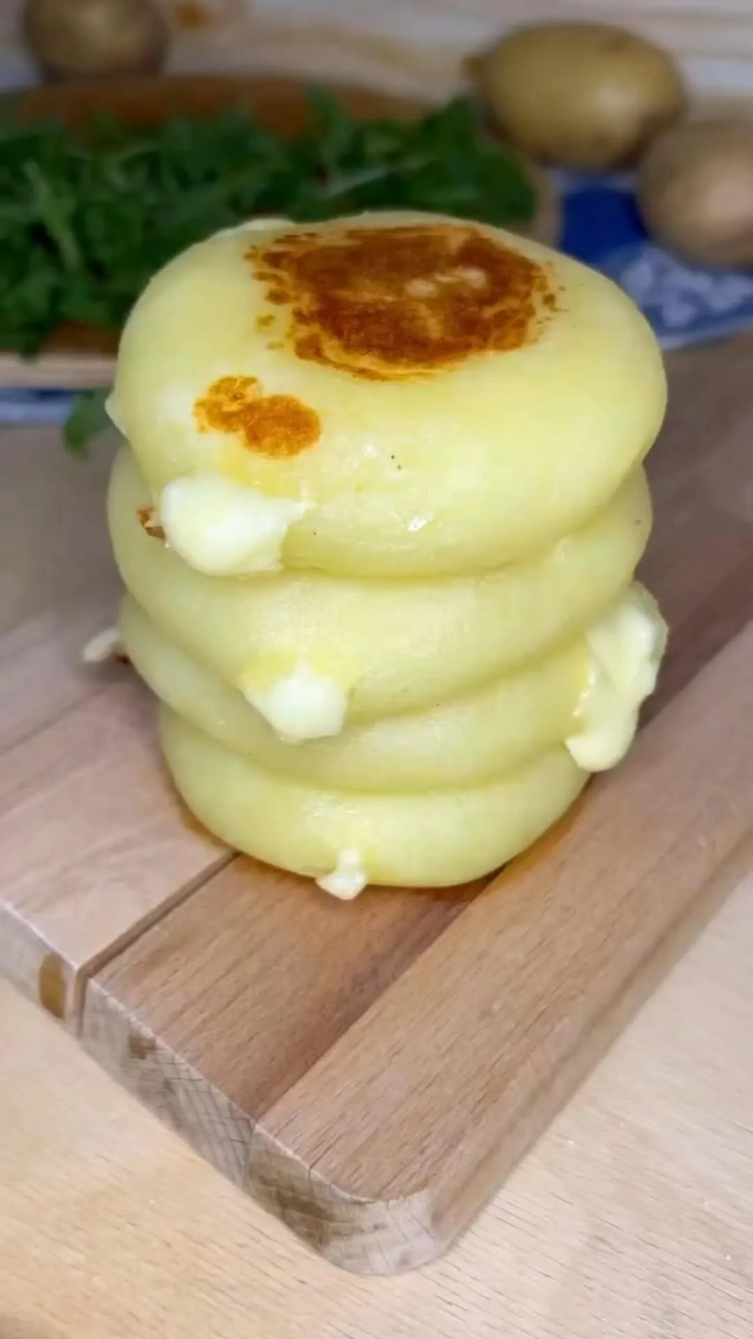 Ein Stapel von vier goldbraun gebratenen Kartoffelpuffern mit schmelzendem Käsekern auf einem Holzbrett.