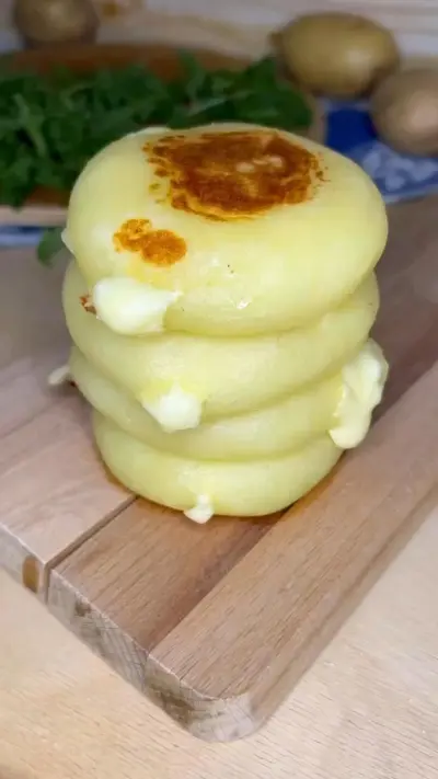 Une pile de quatre galettes de pommes de terre dorées contenant du fromage fondant sur une planche en bois.