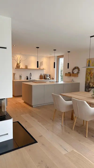 Eine moderne, offene Küche in hellgrauen Tönen mit Kücheninsel, Eichenparkett und einem angrenzenden Holzesstisch.