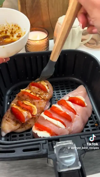 Zwei Hähnchenbrustfilets werden in einem Heißluftfritteusen-Korb mit einer Marinade bepinselt.