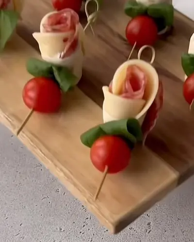 Brochettes apéritives composées de tomates cerises, de basilic et de fleurs formées de fromage et de charcuterie.